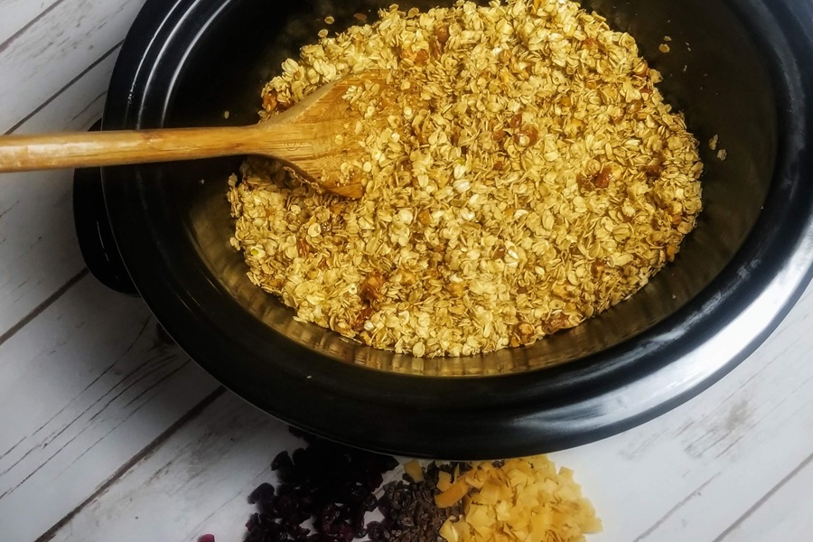 Crockpot Gluten Free Granola Recipe View of a Crockpot with Granola Inside and a Wooden Spoon Sticking Out