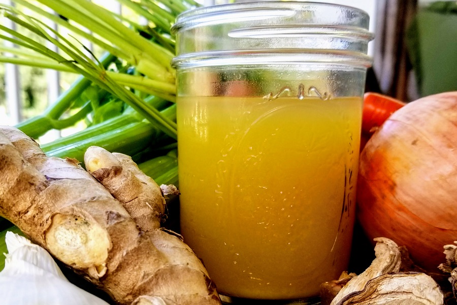 Slow Cooker Chicken Bone Broth Recipe Front View of Broth in a Glass Jar Surrounded with Veggies