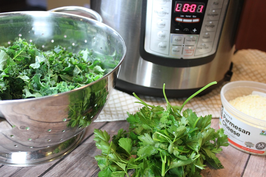 Easy Creamy Kale Soup an Instant Pot with a Colander Filled with Kale in Front of it and Some Parsley Next to a Small Dish of Parmesan Cheese 