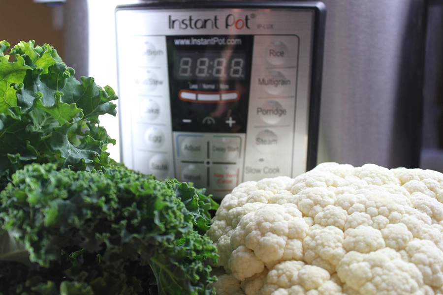 Easy Creamy Kale Soup Close Up of a Bundle of Kale and a Head of Cauliflower in Front of an Instant Pot