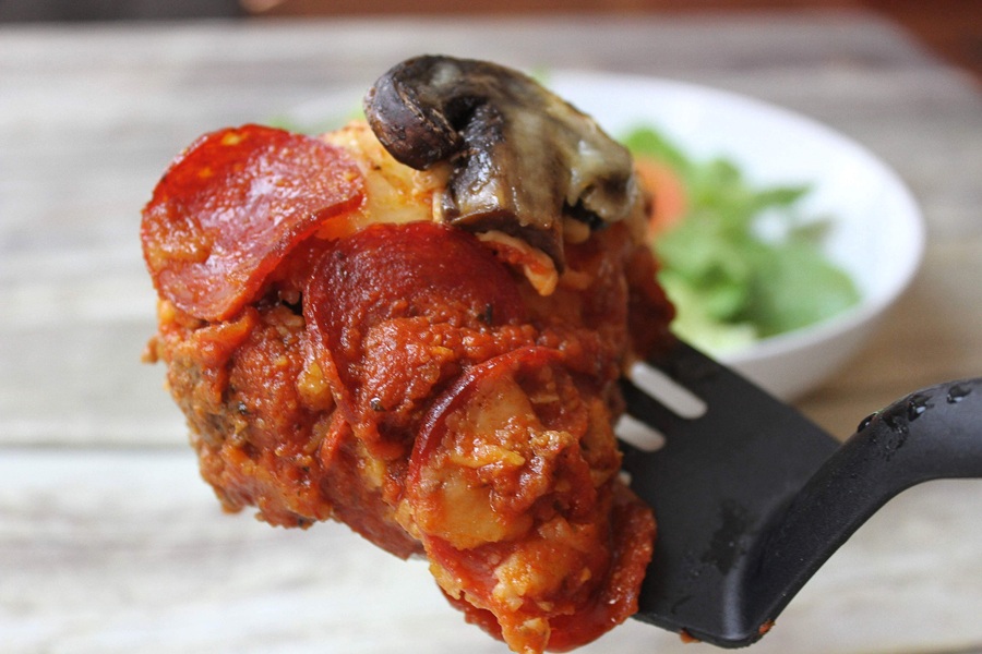 Crock Pot Pizza Casserole on a Spatula with a White Bowl of Salad in the Background