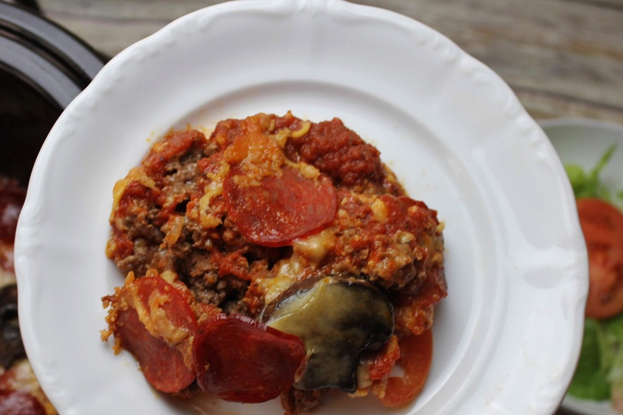 Crock Pot Pizza Casserole on a White Plate Above a Crock Pot and a Salad