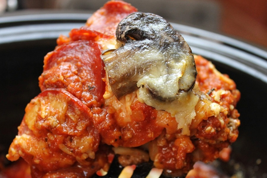 Crock Pot Pizza Casserole on a Spatula Being Held Above a Crock Pot Filled with Casserole