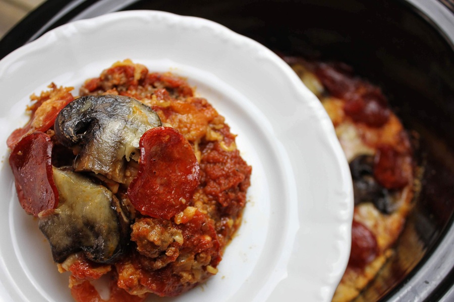 Crock Pot Pizza Casserole on a White Plate Being Held Above a Crock Pot