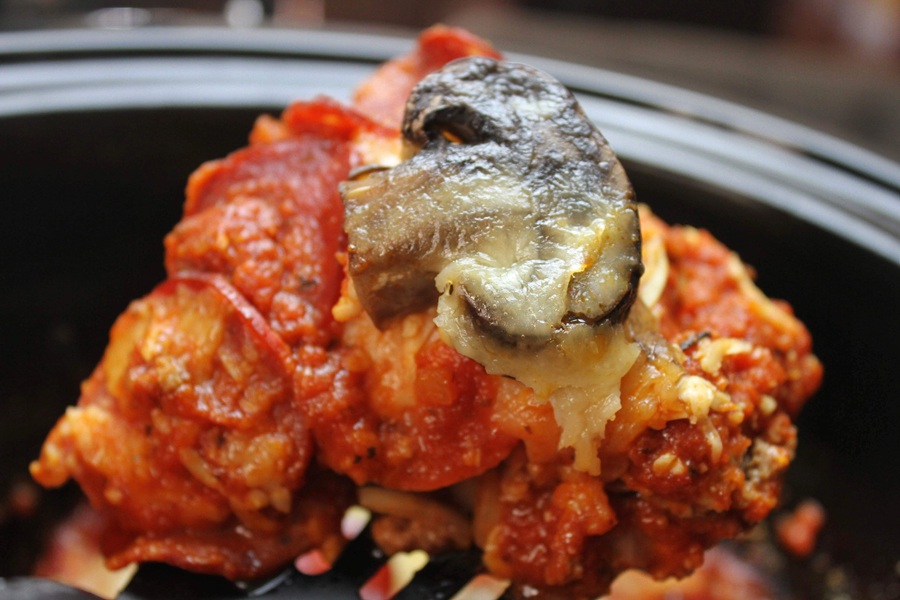 Crock Pot Pizza Casserole Close Up of a Serving of Pizza Casserole on a Spatula Hovering Above a Crock Pot