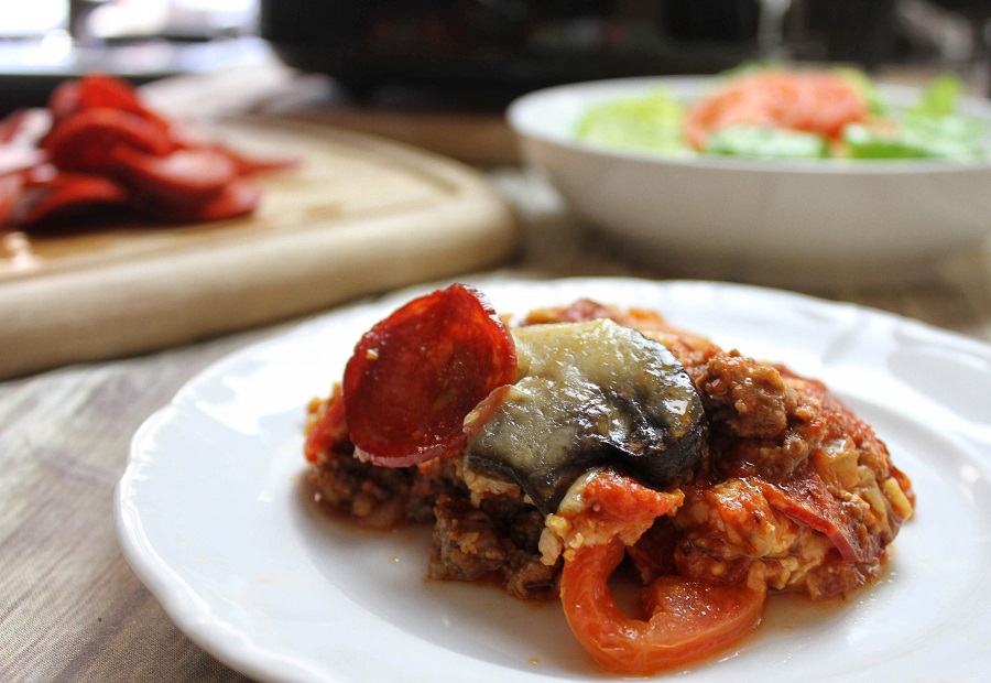 Crockpot Pizza Recipes Casserole on a Plate with a Bowl of Salad in the Background