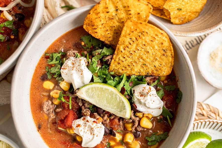 Crockpot Taco Soup Recipe Overhead View of a Bowl of Taco Soup Garnished with Sour Cream, Lime Wedges, and Tortilla Chips