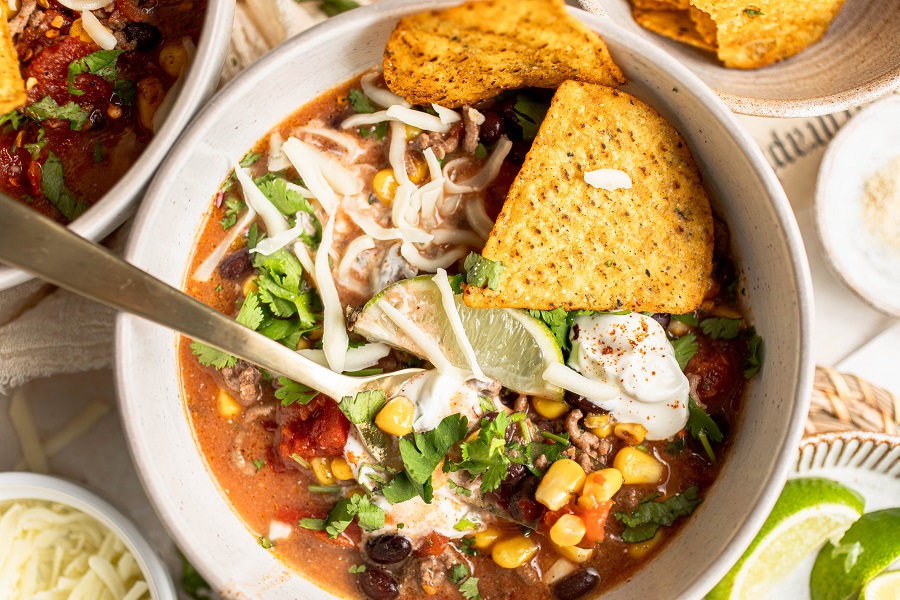 Crockpot Taco Soup Recipe Overhead View of a Bowl of Taco Soup with a Fork and Garnished with Tortilla Chips and Limes