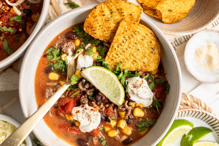 Crockpot Taco Soup Recipe Close Up of a Bowl of Taco Soup Garnished with Sour Cream, Limes and Tortilla Chips