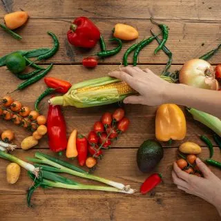 Instant Pot Corn Recipes Assorted Veggies on a Wooden Surface with a Hand Grabbing for the Corn