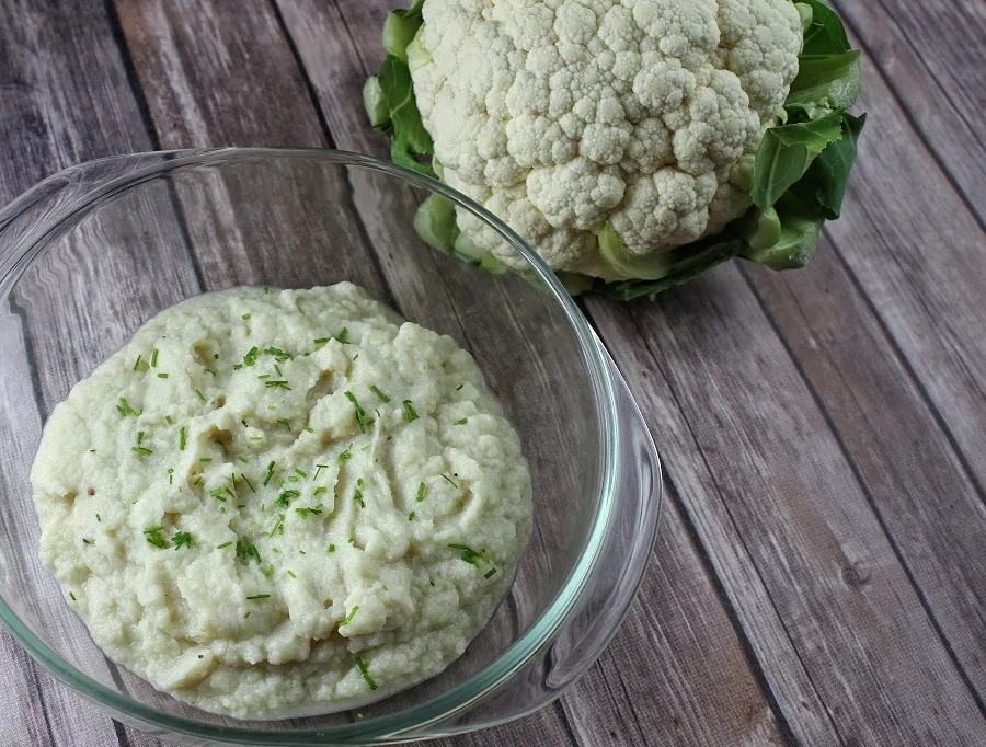 Instant Pot Thanksgiving Recipes for Dessert Angled View of a Bowl of Mashed Cauliflower with a Head of Cauliflower Next to the Bowl