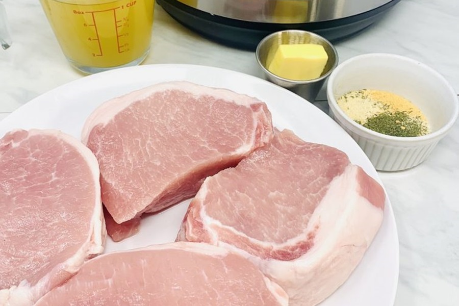 Instant Pot Frozen Pork Chops Raw Pork Chops on a Plate with Oil, Chicken Stock, and Seasonings in the Background