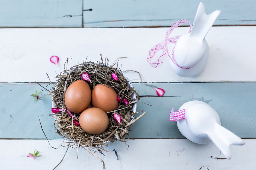 Easy Crockpot Easter Recipes Overhead View of a Nest with Three Eggs Inside and Two Glass Bunny Figures to the Side