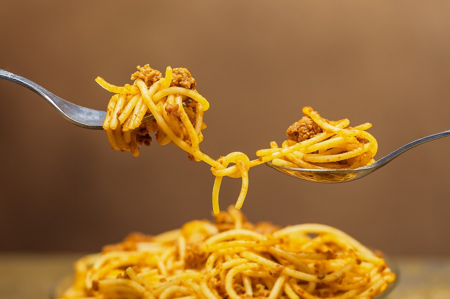How to Cook Pasta in the Instant Pot Close Up of Spaghettie and Meat Sauce Balanced Between Two Forks Above a Plate of Pasta