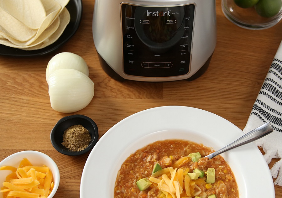 Instant Pot Ace Blender Tips and Tricks Bowl of Chili in Front of an Ace Blender on a Wooden Surface with Seasonings and Ingredients Sitting Next to Them