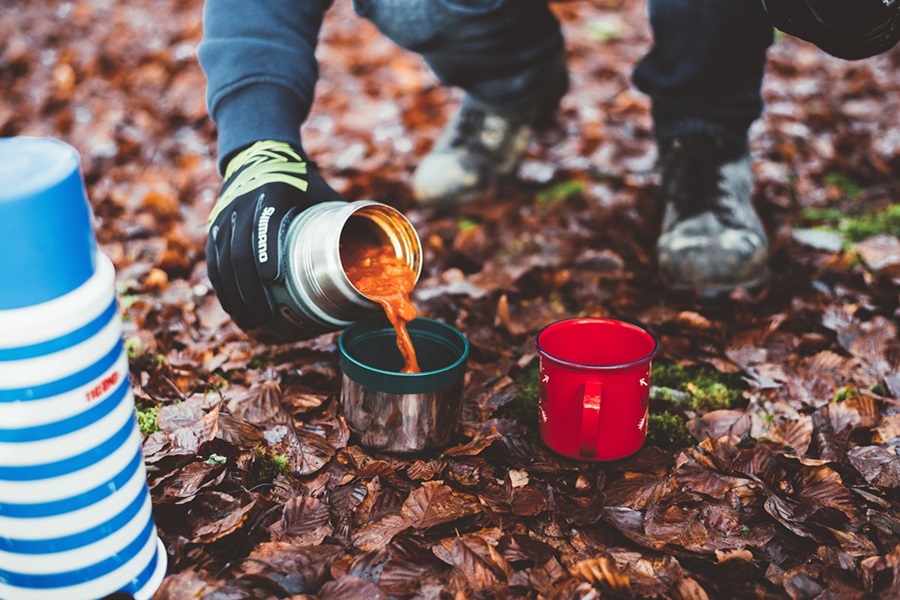 Best Crockpot Recipes for Camping Close Up of a Person Pouring Soup From a Cannister into a Small Cup on a Hiking Trail