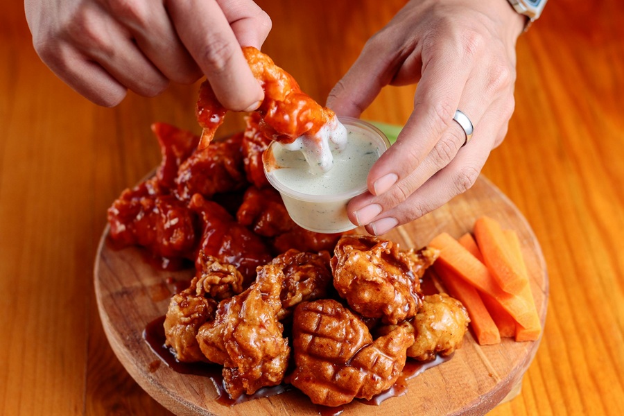 Super Bowl Appetizers Close Up of a Person Dipping a Hot Wing into a Small Ramekin of Ranch