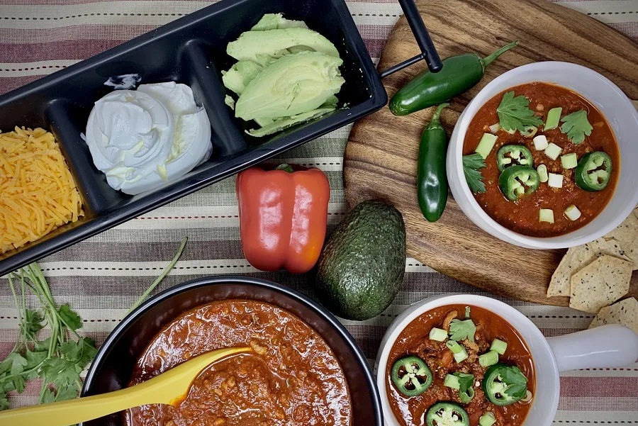 Instant Pot Meal Prep Recipes for Spring Overhead View of a Bowl of Chili Next to an Array of Toppings Like Sour Cream, Avocado, and Cheese