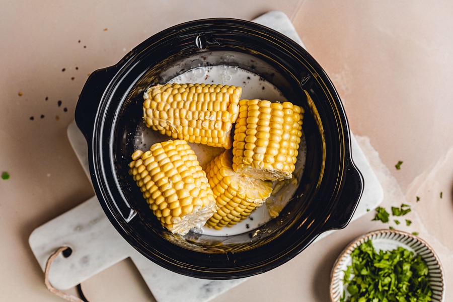 Crockpot Corn on the Cob with Coconut Milk Recipe Overhead View of a Crockpot with Cobs Inside and Other Ingredients Added