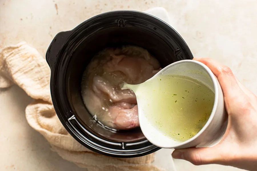 Slow Cooker Chicken and Spinach Rice Bowl Recipe View of a Crockpot with a Person Pouring Chicken Broth Into the Crockpot