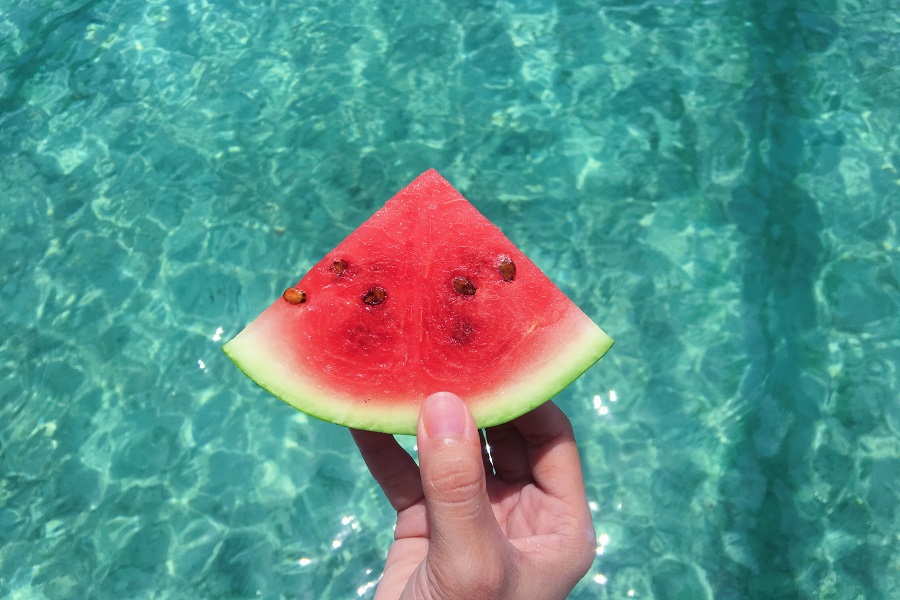 Summer Bod Memes Close Up of a Person's Hand Holding a Slice of Watermelon Over a Pool