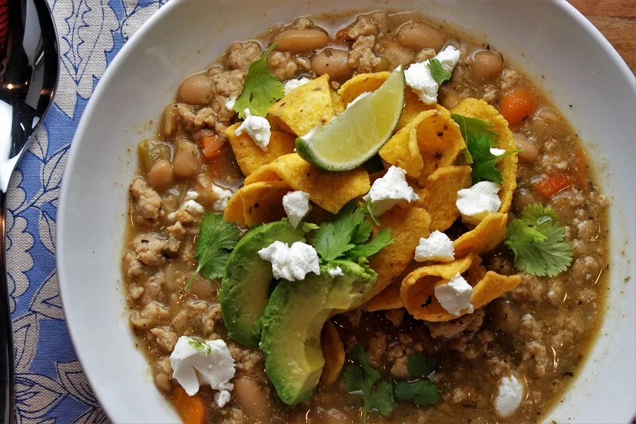 Dorm Room Crockpot Recipes Close Up of a Bowl of Chicken Chili Garnished with Avocado, Frito Chips, and Parsley 