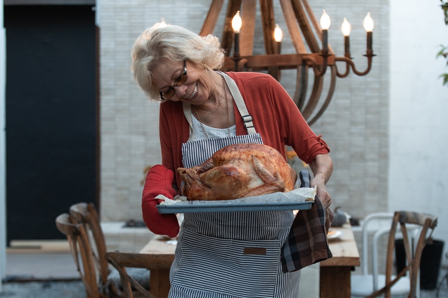 How to Smoke a Turkey in a Propane Smoker a Woman Carrying a Cooked Turkey on a Platter with a Table Behind Her