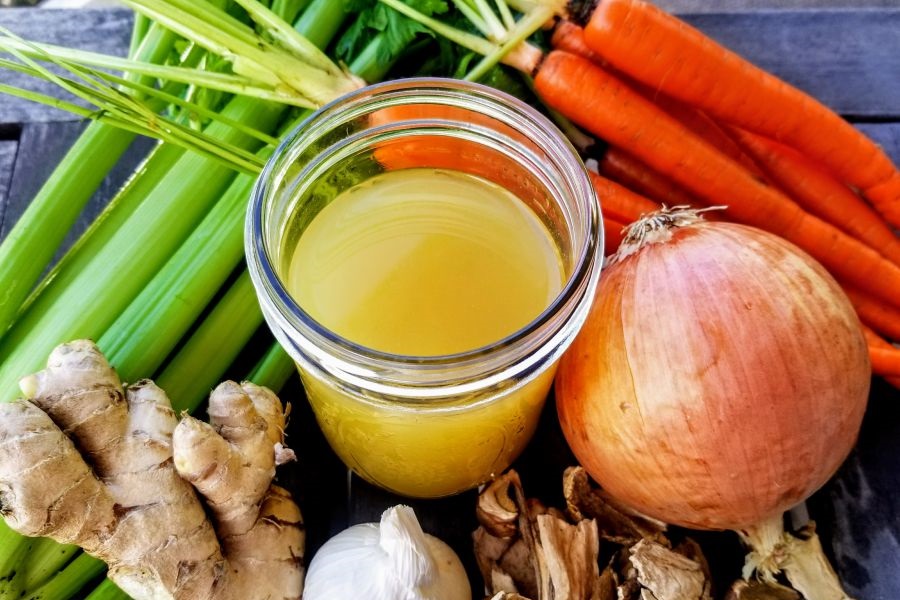 Keto Chicken Bone Broth Recipe a Jar of Chicken Bone Broth Surrounded by Carrots, Celery, Ginger, Onions, and Garlic