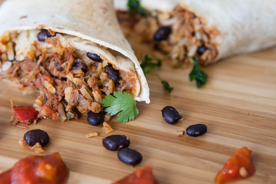 Mexican Barbacoa Recipe Ideas a Burrito Cut in Half with Black Beans, Shredded Meat, and Tomatoes Spilling Out from Each Half