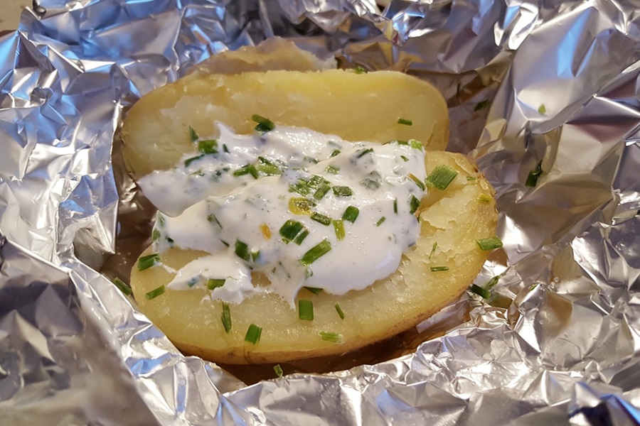 Baked Potatoes in the Oven Close Up of a Baked Potato Cut in Half Topped with Sour Cream and Chives on Foil
