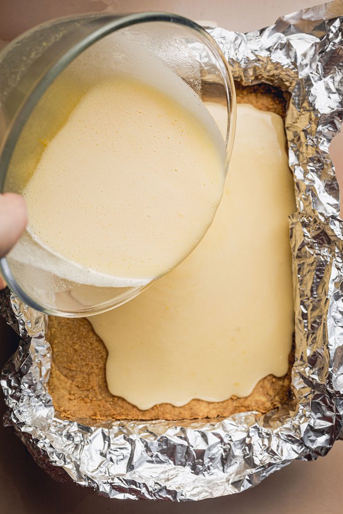 Easy Lemon Bars Recipe a Bowl of Lemon Filling Mixture Being Poured On To a Crust in a Pan