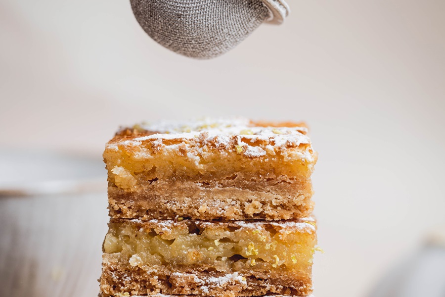 Easy Lemon Bars Recipe a Stack of Lemon Bars with a Sugar Sifter Floating Above