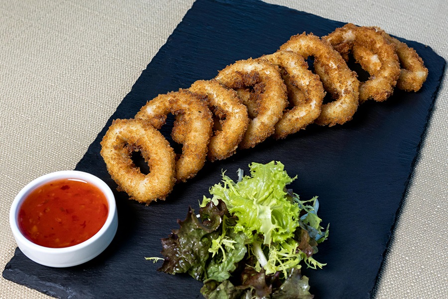 How to Reheat Calamari in an Air Fryer a Black Cutting Board with Calamari Rings and a Small Bowl of Dipping Sauce