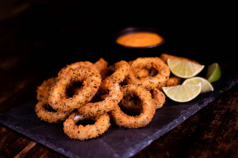How to Reheat Calamari in an Air Fryer a Black Cutting Board with Calamari with Lime Wedges and a Orange Dipping Sauce