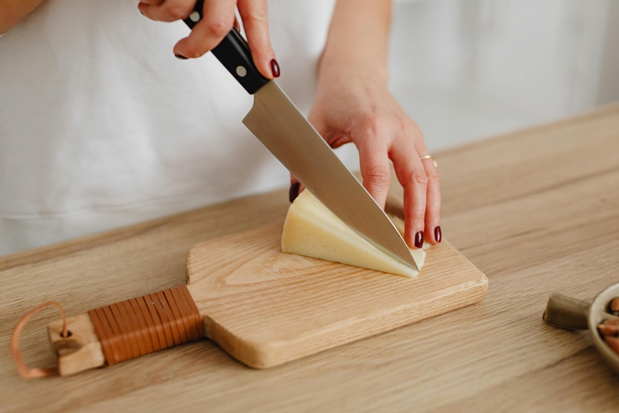 Recipes with Queso Dip Close Up of a Person Cutting Cheese into Wedges on a Wooden Cutting Board