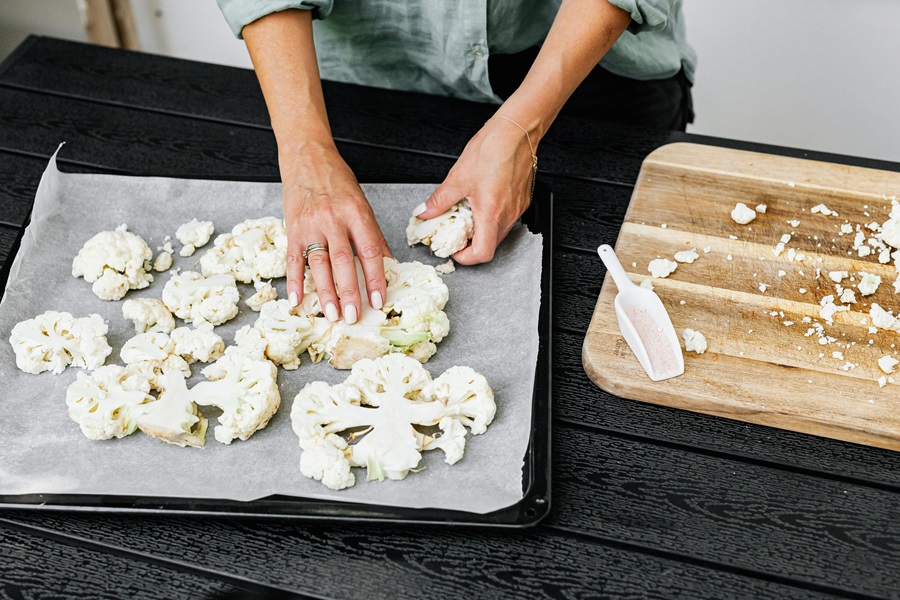 Instant Pot Cauliflower Recipes Close Up of a Person Cutting Up Cauliflower and Placing it on Parchment Paper