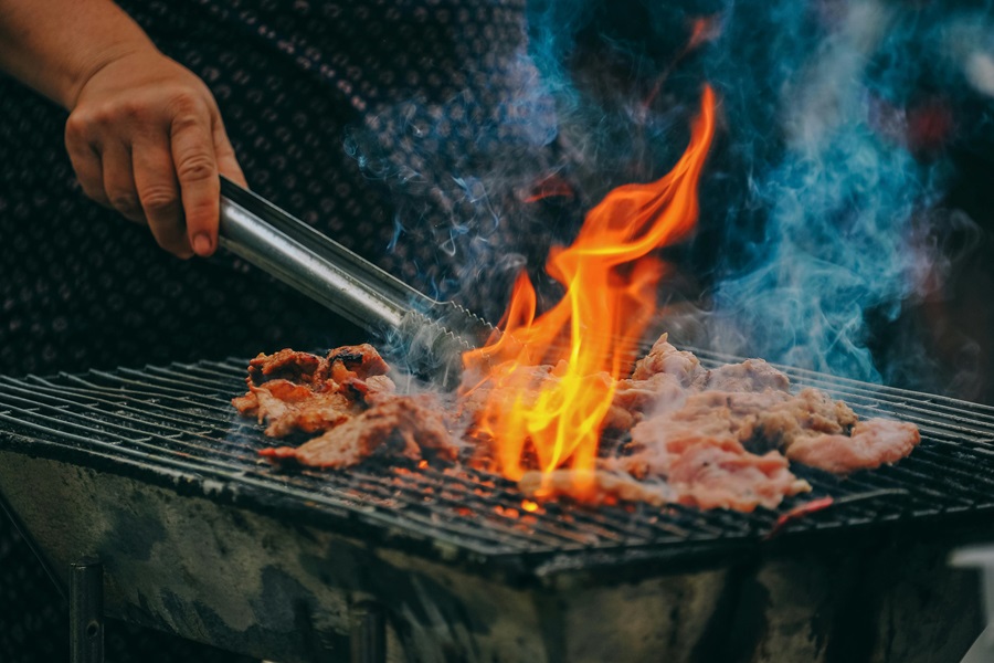 Summer Dinner Recipes for the Grill Close Up of Flames Bursting Out from a Grill with a Person Flipping Meat Using Tongs