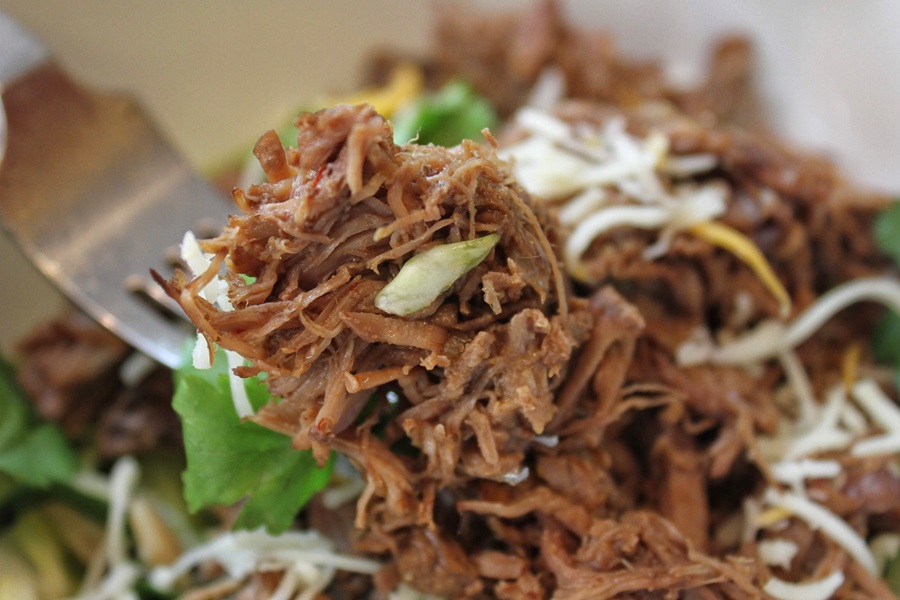 Easy Crockpot Beef Barbacoa Close Up of Barbacoa on a Fork Above a Small White Bowl