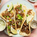 Easy Crockpot Beef Barbacoa a Plate with Three Beef Barbacoa Tacos Topped with Cilantro and Lime Wedges