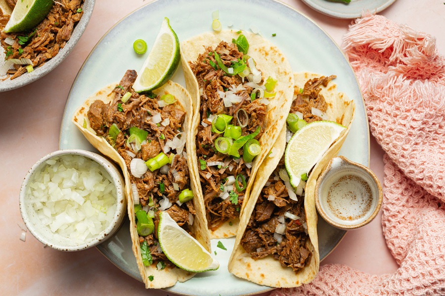 Easy Crockpot Beef Barbacoa a Plate with Three Beef Barbacoa Tacos Topped with Cilantro and Lime Wedges