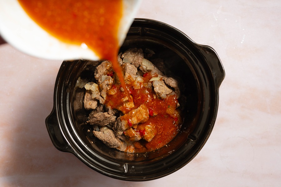 Easy Crockpot Beef Barbacoa Beef in a Crockpot with a Person Pouring the Sauce Into the Crockpot