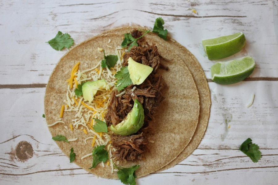 Easy Crockpot Beef Barbacoa Overhead View of a Tortilla Topped with Barbacoa, Avocado, Cheese, and Cilantro