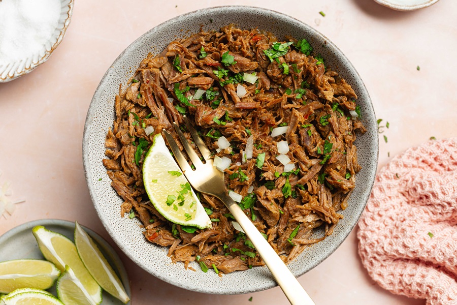 Easy Crockpot Beef Barbacoa on a Plate with a Fork and a Lime Wedge