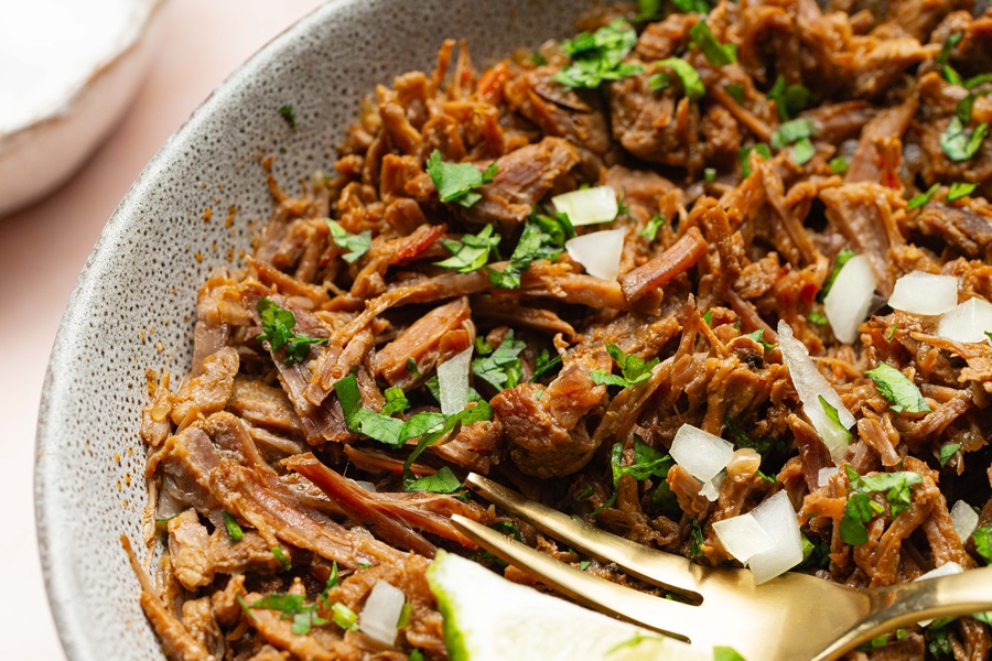 Easy Crockpot Beef Barbacoa Close Up of Beef Shredded with a Fork and Topped with Onions and Cilantro