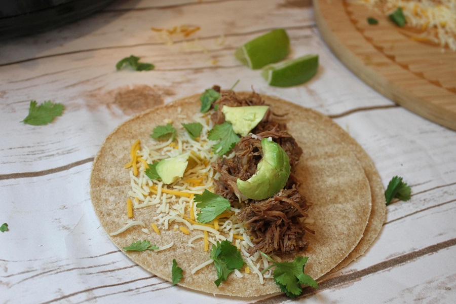 Easy Crockpot Beef Barbacoa on a Corn Tortilla with Avocado Slices, Shredded Cheese, and Cilantro