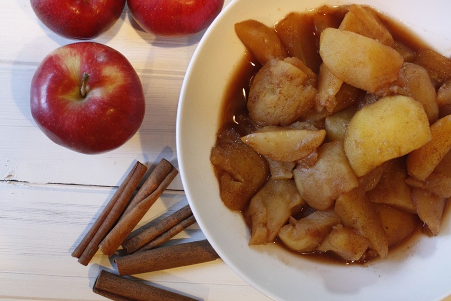 Faster than Stovetop Instant Pot Cinnamon Apples Recipe a Bowl of Cinnamon Apples Next to Red Apples and Sticks of Cinnamon on a Wooden Surface