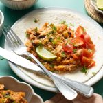 Easy Chicken Tacos in the Slow Cooker a Tortilla Topped with a Chicken Mixture Tomatoes, and a Lime Wedge on a Plate