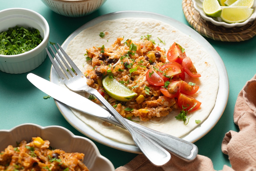 Easy Chicken Tacos in the Slow Cooker a Tortilla Topped with a Chicken Mixture Tomatoes, and a Lime Wedge on a Plate