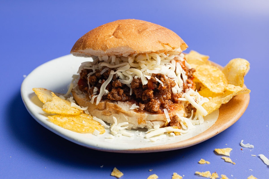 Crockpot Sloppy Joes Recipe Close Up of a Sloppy Joe Topped with Cheese on a Plate with Chips