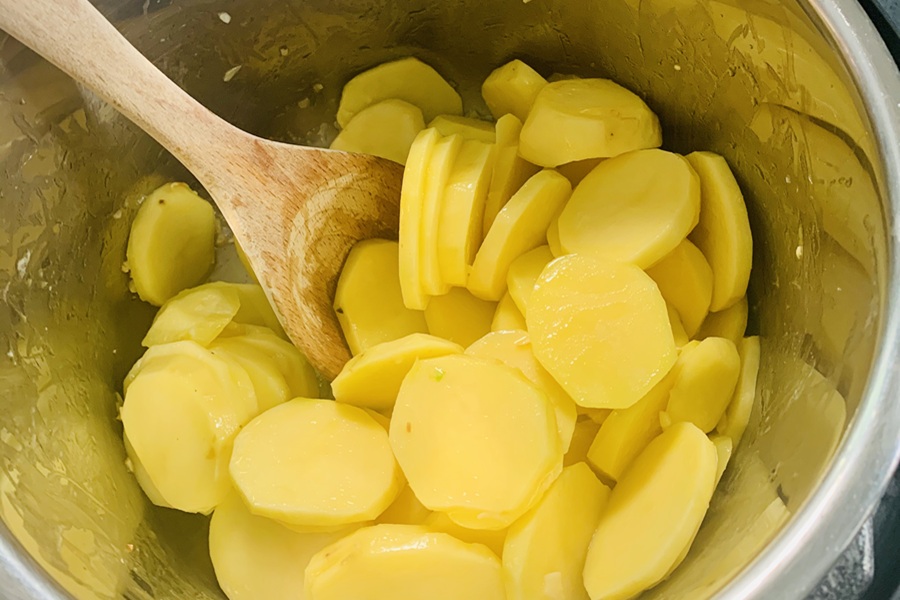 Easy Instant Scalloped Potatoes Sliced Potatoes in an Instant Pot with a Wooden Spoon
